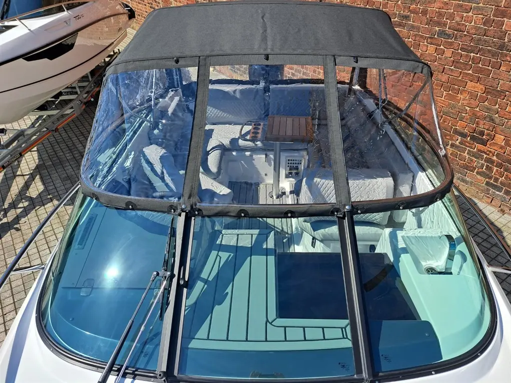 A top view of a boat with a black canopy, showing cushioned seating and a wooden table on the deck beside a brick wall.